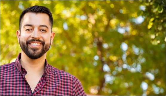 Man in red and black plaid shirt smiling outdoors