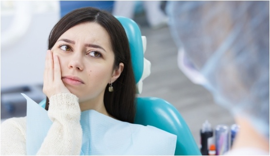 Woman in dental chair holding her cheek in pain