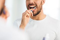 Nose-to-chest view of man in white shirt brushing teeth in front of mirror