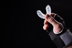Hand in fingerless glove holding translucent mouthguard with black background