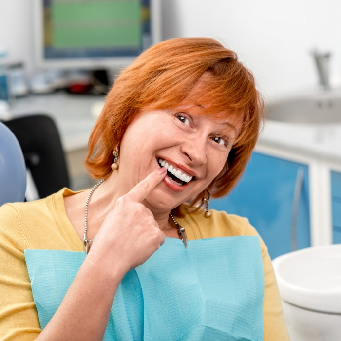 Woman in dental chair pointing to her smile