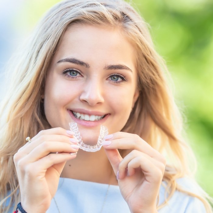 Smiling blonde woman holding an Invisalign aligner