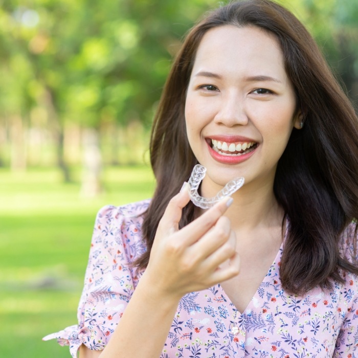 Smiling woman holding a clear aligner outdoors
