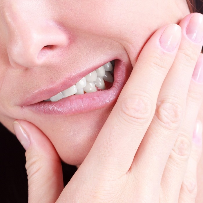 Close up of wincing person holding their cheek in pain before tooth extractions in Plattsburgh