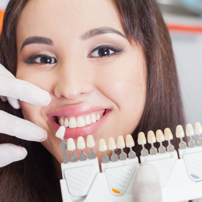 Woman smiling next to shade guide for dental veneers in Plattsburgh